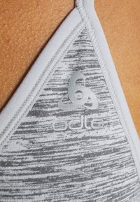 Soutien-gorge de sport gris avec un motif texturé, un bord blanc et un logo argenté. Le matériau semble lisse avec une finition douce.