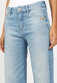 Light blue jeans made of denim, featuring a classic five-pocket design, subtle distressing, and a metal button closure at the waist.