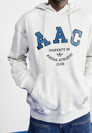 Sudadera gris con "AAC" en azul en el pecho, con "PROPIEDAD DEL CLUB ATLÉTICO ADIDAS" en negro, cordones y un bolsillo delantero.