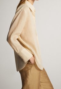 Ljusbeige långärmad blus i lätt tyg, med klassisk krage och en något böjd fåll.
