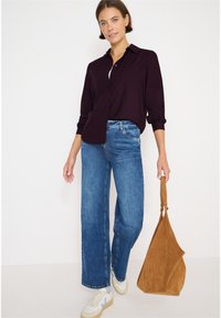 Mørklilla skjorte med knapper, mellemblå vide jeans, hvide sneakers med lyse accenter og en brun ruskinds håndtaske. Afslappet outfit.
