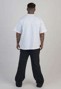 Balta kokvilnas T-krekls ar apaļu kakla izgriezumu un īsām piedurknēm, apvienots ar brīviem melniem biksēm. Apģērbs ir ar brīvu piegriezumu un minimālu dizainu.