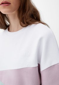 Mikina s kulatým výstřihem v bílých, světle růžových a mátově zelených částech. Texturovaná tkanina s jemně vyraženým logem na hrudi.