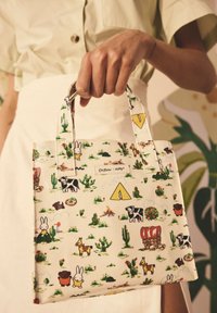 Hvid tote bag med et legesyndigt mønster af køer, kaniner og kaktuser. Den har to håndtag og et mærke. Fremstillet af slidstærkt materiale.