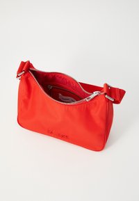 Rød nylon skulderveske med glidelåslukking, med en enkelt stropp og preget logo på forsiden, som viser en jevn tekstur.