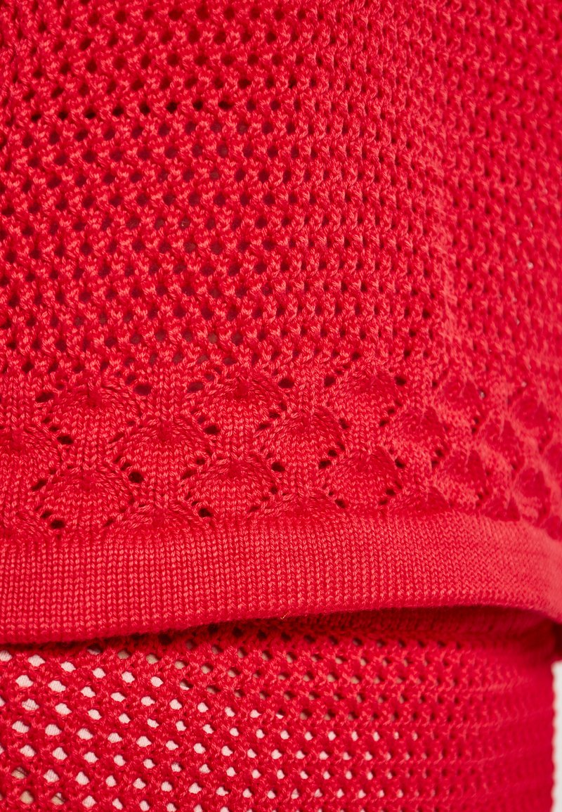 Roter gestrickter Stoff mit einem strukturierten Muster mit kleinen Löchern, geschichtetem Design und einem gewellten Rand. Das Material wirkt weich und flexibel.