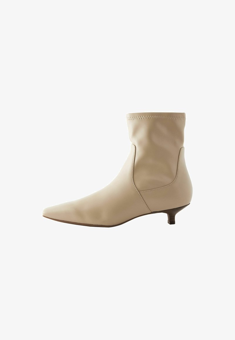 Bottine en cuir beige à bout pointu, avec une tige souple et un petit talon bloc, présentant un design sans couture et un minimum de détails de couture.