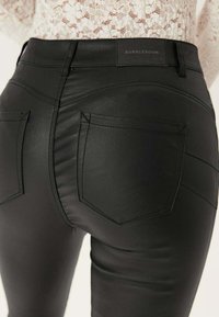 Pantaloni in finta pelle nera con design aderente, cuciture visibili e due tasche posteriori. Etichetta del marchio "BUBBLEROOM" sulla parte posteriore della vita.