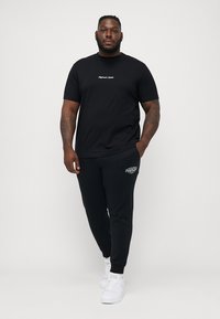 Černé bavlněné tričko s bílým logem, spárované s černými teplákovými kalhotami s malým logem a bílými teniskami. Jednoduchý, neformální outfit.