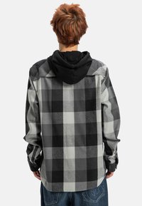 Camisa de franela a cuadros en negro y gris, con una capucha negra adjunta, puños de botón y una textura suave.