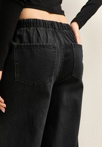 Czarne dżinsowe spodnie z elastycznym pasem, posiadające dwie tylne kieszenie i luźny krój. Tekstura jest nieco szorstka, z matowym wykończeniem.