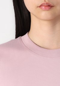 Jasnoróżowa bawełniana koszula z krótkim rękawem z prążkowanym okrągłym dekoltem. Gładka struktura i minimalne detale przeszycia na dekolcie.