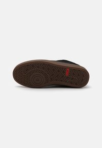 Black sneaker bottom view featuring a textured rubber outsole with a herringbone pattern and a circular detail. Red "GLOBE" label visible.
