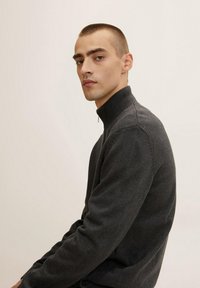 Tmavě šedý pletený svetr s vysokým límcem a zipovým uzávěrem, s texturovaným povrchem a žebrovanými manžetami.