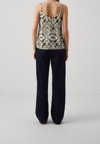 Top in camicia con un motivo beige e oliva, con spalline sottili, abbinato a jeans a gamba larga di colore blu scuro, che presentano una vestibilità rilassata.