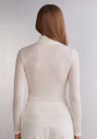 Ribbade polotröja i ljus beige, med långa ärmar och en figursydd siluett, med en slät yta och subtil färggradering.