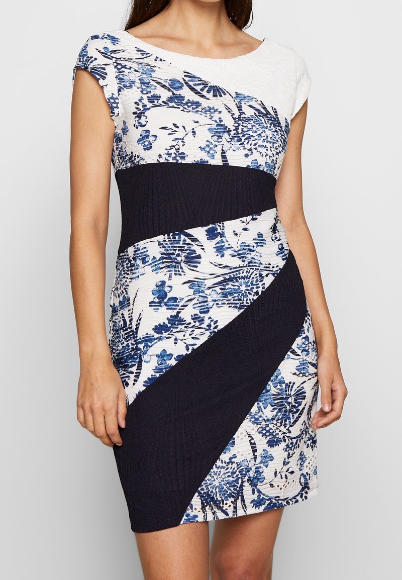 Robe à motif floral avec un haut blanc et une bande texturée bleu foncé autour de la taille. Accent en bleu et blanc avec une silhouette ajustée.