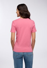 T-shirt in cotone rosa con maniche corte, scollo rotondo e silhouette aderente, abbinata a jeans blu con tasche posteriori.