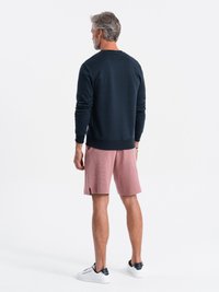 Marineblauwe sweatshirt met ribgebreide manchetten en onderkant, gecombineerd met lichtroze shorts met een gestructureerd patroon en zijsplitten. Witte sneakers maken de look compleet.