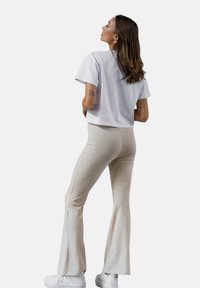 Przycięta jasnoszara koszulka i beżowe spodnie dzwonowe, obie wykonane z miękkiego materiału, połączone z białymi butami sportowymi. Gładka tekstura z casualowym krojem.