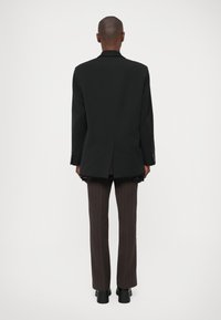 Blazer negro ajustado con solapas de muesca, ventilación trasera y pantalones a rayas marrones a juego. Textura suave y diseño estructurado.
