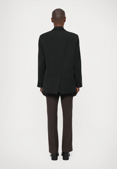Sacou negru croit, cu reveruri tăiate, ventral la spate și pantaloni cu dungi maro asortate. Textură netedă și design structurat.