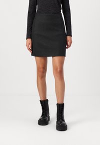 Falda negra hecha de una tela texturizada, con una silueta ajustada, bolsillos laterales y un dobladillo por encima de la rodilla, combinada con botas negras gruesas.