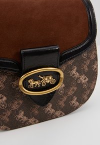 Borsa in suede marrone e pelle nera testurizzata con hardware in metallo dorato a forma di cavallo e carro, dalla forma curvata e superficie decorata.
