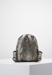 Mochila hecha de textura gris de piel de serpiente sintética, con correas ajustables, forma redondeada y un sutil patrón decorativo.