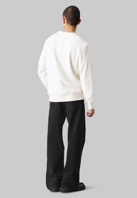 Felpa bianca con collo e polsini a costine, abbinata a pantaloni neri a gamba larga. Il tessuto sembra morbido con una superficie liscia.