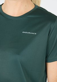 Mörkgrön träningströja i ett mjukt och slätt material. Har rund hals och ordet "ENDURANCE" i vitt på framsidan.