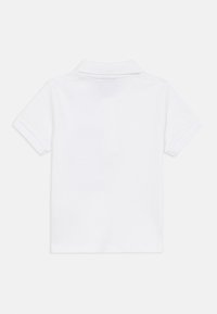 Λευκό πόλο μπλουζάκι με κοντά μανίκια, κλασικό γιακά, κατασκευασμένο από λείο ύφασμα. Απλός σχεδιασμός χωρίς πρόσθετα σχέδια ή διακοσμητικά στοιχεία.