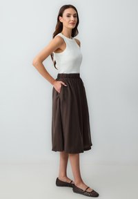 Top bianco senza maniche con scollatura rotonda abbinato a una gonna marrone di lunghezza media con vita elasticizzata e tasche laterali. Scarpe basse nere.