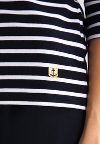 Granatowa i biała bluzka w paski, z małym haftowanym logo w kolorze żółtym i niebieskim. Wykonana z miękkiej bawełny, o dopasowanym kroju i krótkich rękawach.