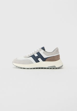 Lage sneakers in wit, grijs, bruin suède en marineblauw leer met een dikke witte zool en witte veters, zijaanzicht op een effen achtergrond.
