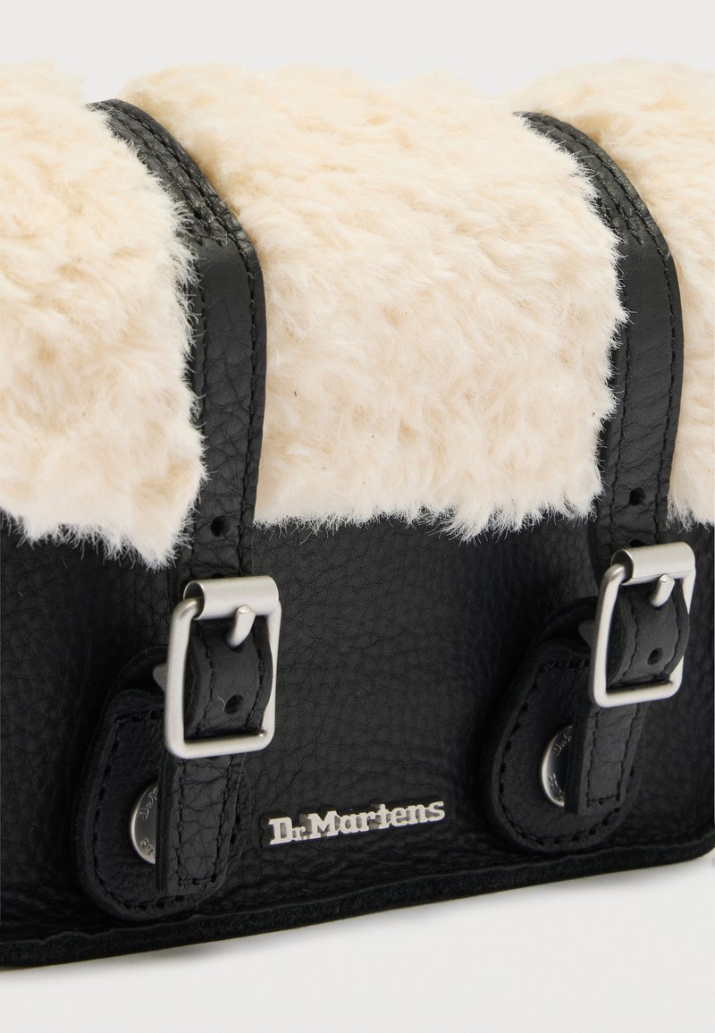 Schwarze Lederhandtasche mit strukturierter Oberfläche, cremefarbener Schaffell-Klappe, zwei silbernen Schnallen und Metall-Logo "Dr. Martens" vorne.