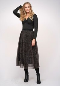Top nero a maniche lunghe con design frontale attorcigliato abbinato a una gonna maxi trasparente con stampa leopardata nera, completato da stivali neri alla caviglia.