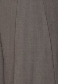 Pantalon gris sur mesure en tissu texturé avec plis et coutures apparents, présentant une finition lisse et une coupe droite.