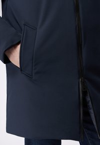 Marineblauer wasserdichter Mantel mit Reißverschluss, Seitentasche, glatter Textur und knielangem Design. Geeignet für verschiedene Wetterbedingungen.