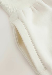 Primer plano de unos pantalones de forro polar color crema que muestran una cintura elástica acanalada y una costura lateral con una abertura vertical para bolsillo.