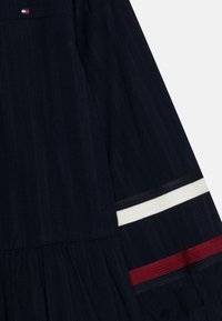 Marineblaues Kleid aus strukturiertem Stoff, mit rot-weiß gestreiften Akzenten an den Ärmeln und einem gerafften Rockdesign.