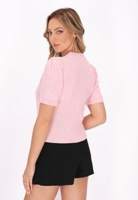 Rosa, kurzärmliges Strickoberteil mit geripptem Saum, strukturiertem Stoff und subtilen Glitzerdetails. Kombiniert mit schwarzen Shorts für einen Kontrast.