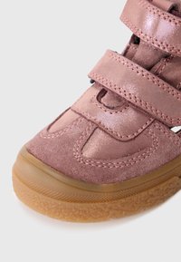 Detailaufnahme eines Sneakers aus pinkem Wildleder und glänzendem Stoff mit zwei Klettverschlüssen und einer strukturierten, hellbraunen Gummisohle.