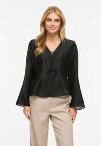 Svart, lett bluse med V-hals og snøring foran. Har lange, flagrende ermer og en løs passform. Jevn tekstur.