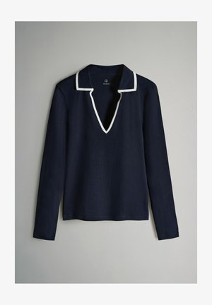 Tamsiai mėlynas ilgomis rankovėmis marškinėliai su V formos iškirpte ir balta apdaila aplink apykaklę. Strukturizuota medžiaga, laisvas siluetas ir tiesus apatinis kraštas.