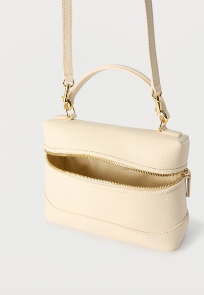 Sac à main en cuir crème avec poignée supérieure et bandoulière amovible, doté d'une fermeture éclair dorée partiellement ouverte sur la poche avant.