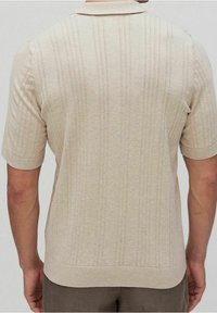Short-sleeve beige knit polo shirt featuring vertical ribbed patterns, a flat collar, and a fitted silhouette. Smooth texture, no graphics.