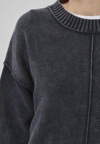 Close-up of a person wearing a dark gray sweater with a ribbed collar, showcasing texture and stitching details.