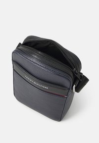 Navy skórzana torba na ramię z teksturowanym wykończeniem, z zamknięciem na zamek błyskawiczny i logo Tommy Hilfiger. Posiada regulowany pasek oraz gładkie akcenty.