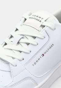 Bílé tenisky s hladkým koženým svrškem, texturovaným jazykem a šněrováním. Výrazné logo Tommy Hilfiger na boku.